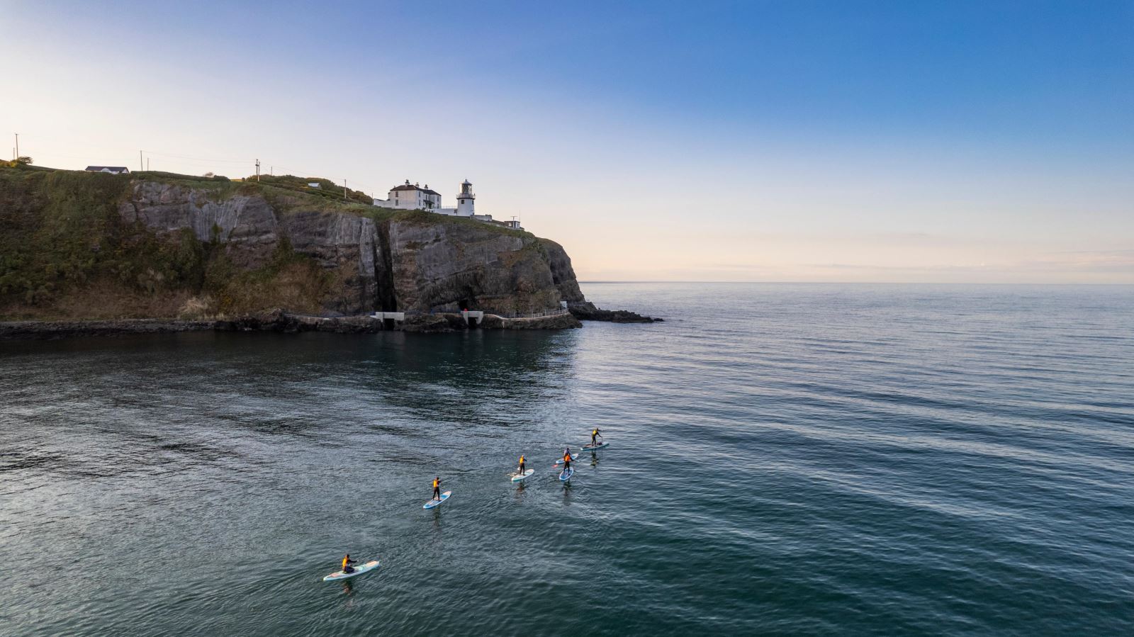 Group of paddleboarders going along coast with Blackhead Lighthouse in background